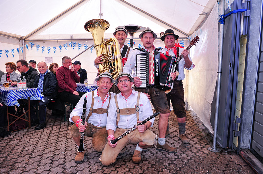 Kleines Bierzelt mit Besuchern auf der linken Seite sowie einer bayerischen Kapelle in der Mitte