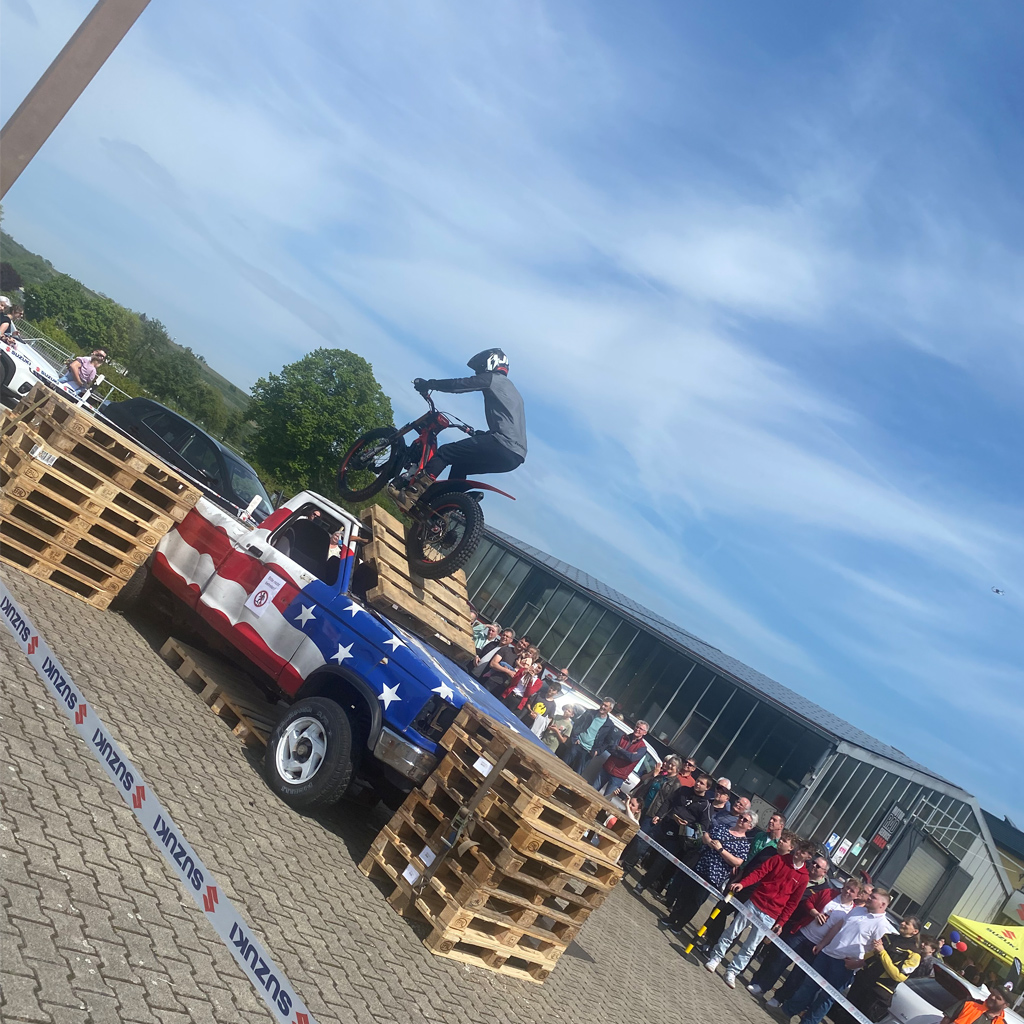 Das Bild zeigt eine Motorradvorführung. Es ist ein Hindernis mit Paletten aufgebaut und im Hintergrund sehen wir einen amerikanischen Truck