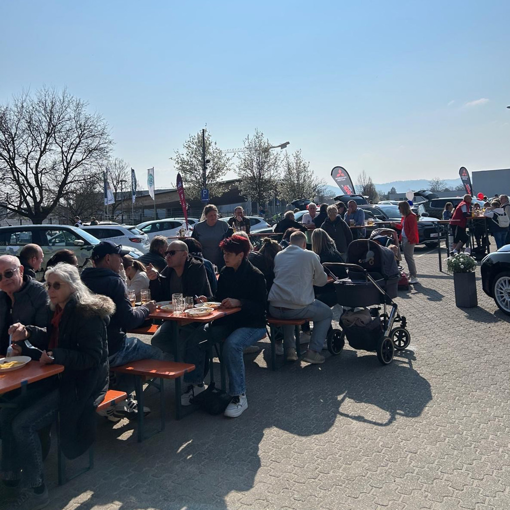 Viele Menschen sitzen ein Biertisch und genießen bei blauen Himmel, den Frühlingstag beim Autohaus Jauch